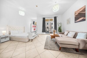 Ein modernes, helles Wohnzimmer mit einem Bett, einer Couch und einem Fernseher auf einem Standfuß.