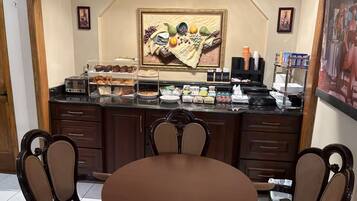 A breakfast bar with various food items, a framed artwork above it, and a dining area with chairs and a table.