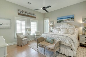 A bedroom with a large bed, two chairs, a small table, a ceiling fan, and artwork on the walls. - Life's Good | Gulf Views | Steps to Beach (Port Aransas)