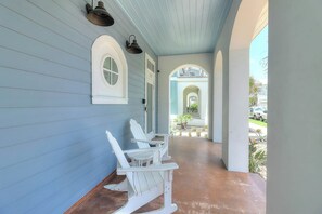 A porch with white rocking chairs, a covered area with a sloped ceiling, and a view of a residential street. - Life's Good | Gulf Views | Steps to Beach (Port Aransas)