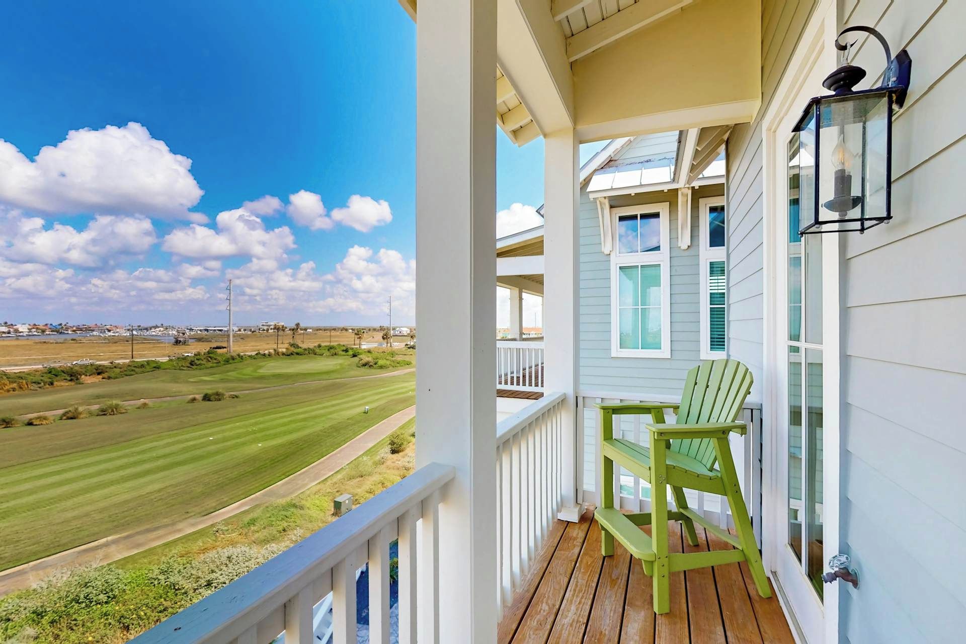 Ein Balkon mit Blick auf einen Golfplatz, ein grüner Stuhl und ein Laternen.