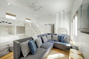 A modern interior with a gray sectional sofa, bunk beds, and a hanging chair. - Kokomo J's | Gulf Views | Steps to Beach (Port Aransas)