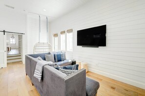 A living room with a grey sofa, a television mounted on the wall, and a wicker chair. - Kokomo J's | Gulf Views | Steps to Beach (Port Aransas)