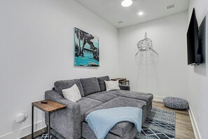 Ein modernes Wohnzimmer mit einem grauen Sofa, einem Gemälde, einem Traumfänger und einem gemusterten Teppich.
