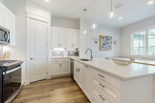 A modern kitchen with white cabinetry, a central island, and a large window providing natural light. - Casita Bonita | Gulf Views | Pet Friendly (Port Aransas)