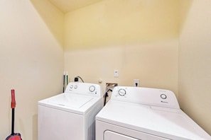 A laundry room with two front-loading washing machines and a red mop. - LUXE Palmilla Home | Gulf Views | Steps to Beach (Port Aransas)