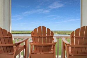 Drie houten Adirondack-stoelen op een balkon met uitzicht op een grasrijk landschap en een wateroppervlak.