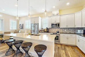 A modern kitchen with white cabinetry, a large island, and black bar stools. - LUXE Palmilla Home | Gulf Views | Steps to Beach (Port Aransas)