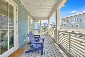 A covered porch with two blue chairs, a wooden floor, and a view of adjacent buildings. - Ocean Haven | Water Views | Private Elevator (Port Aransas)
