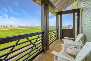 Eine überdachte Veranda mit Blick auf einen Golfplatz, eine Holzterrasse und weiße Adirondack-Stühle.