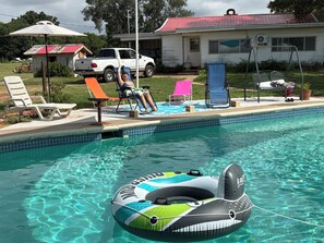 A swimming pool with lounge chairs and a house in the background.