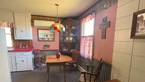 Une cuisine avec des meubles blancs, une table en bois et des chaises. Un luminaire coloré est suspendu au-dessus de la table.