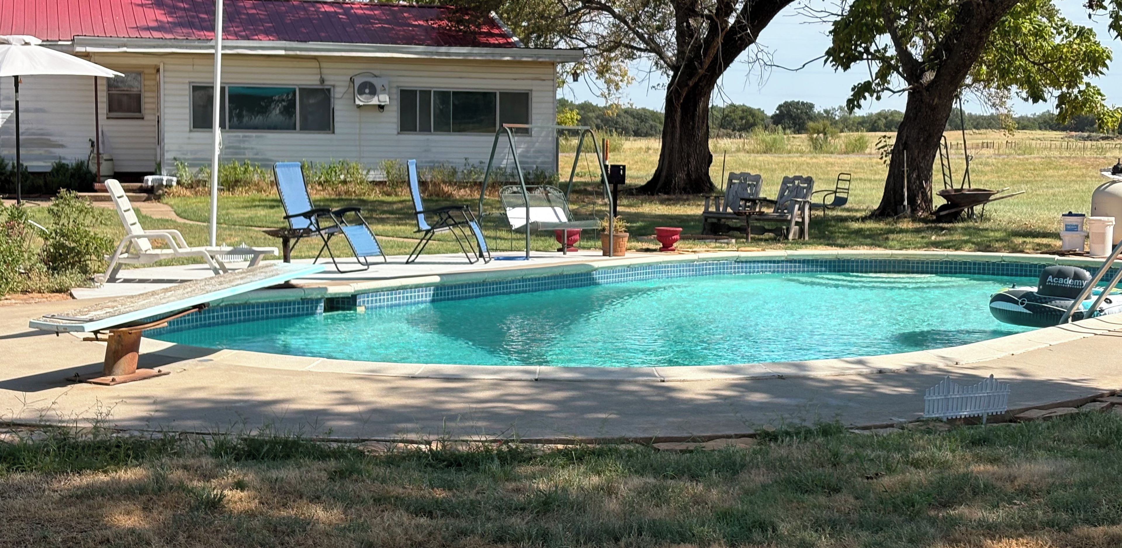 A swimming pool with lounge chairs and a house in the background.