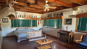Une chambre rustique comprenant un lit, un bureau, une chaise, une tête de cerf accrochée au mur et des trophées exposés sur des étagères.
