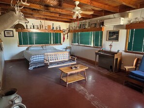 A rustic room with a bed, a desk, a chair, a hanging deer head, and trophies on shelves.
