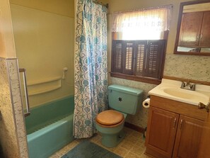A bathroom with a bathtub, toilet, sink, and window with shutters.