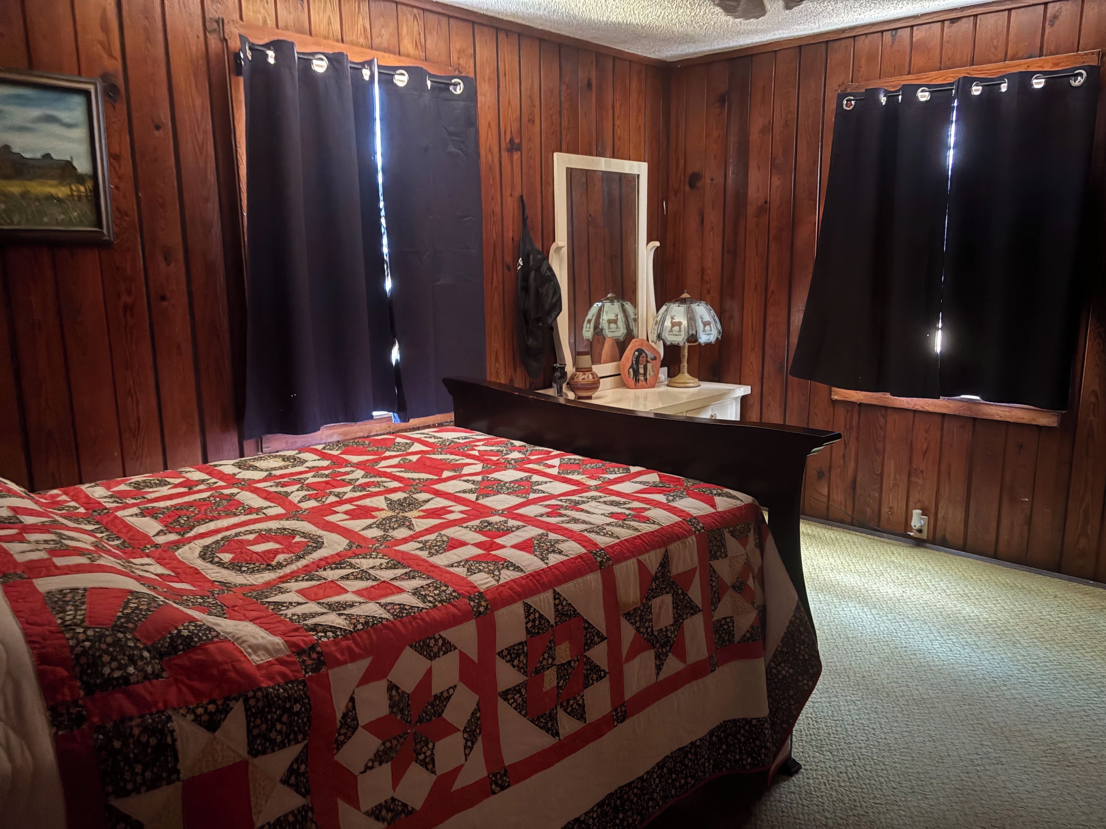 Un dormitorio con pared de paneles de madera, una cama con colcha estampada, un aparador, un espejo y dos lámparas.