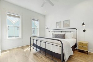 Ein Schlafzimmer mit einem Bett, einem Nachttisch, einer Lampe und zwei Fenstern.