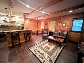 Un interior rústico con barra de madera, zona de estar y pared de piedra.
