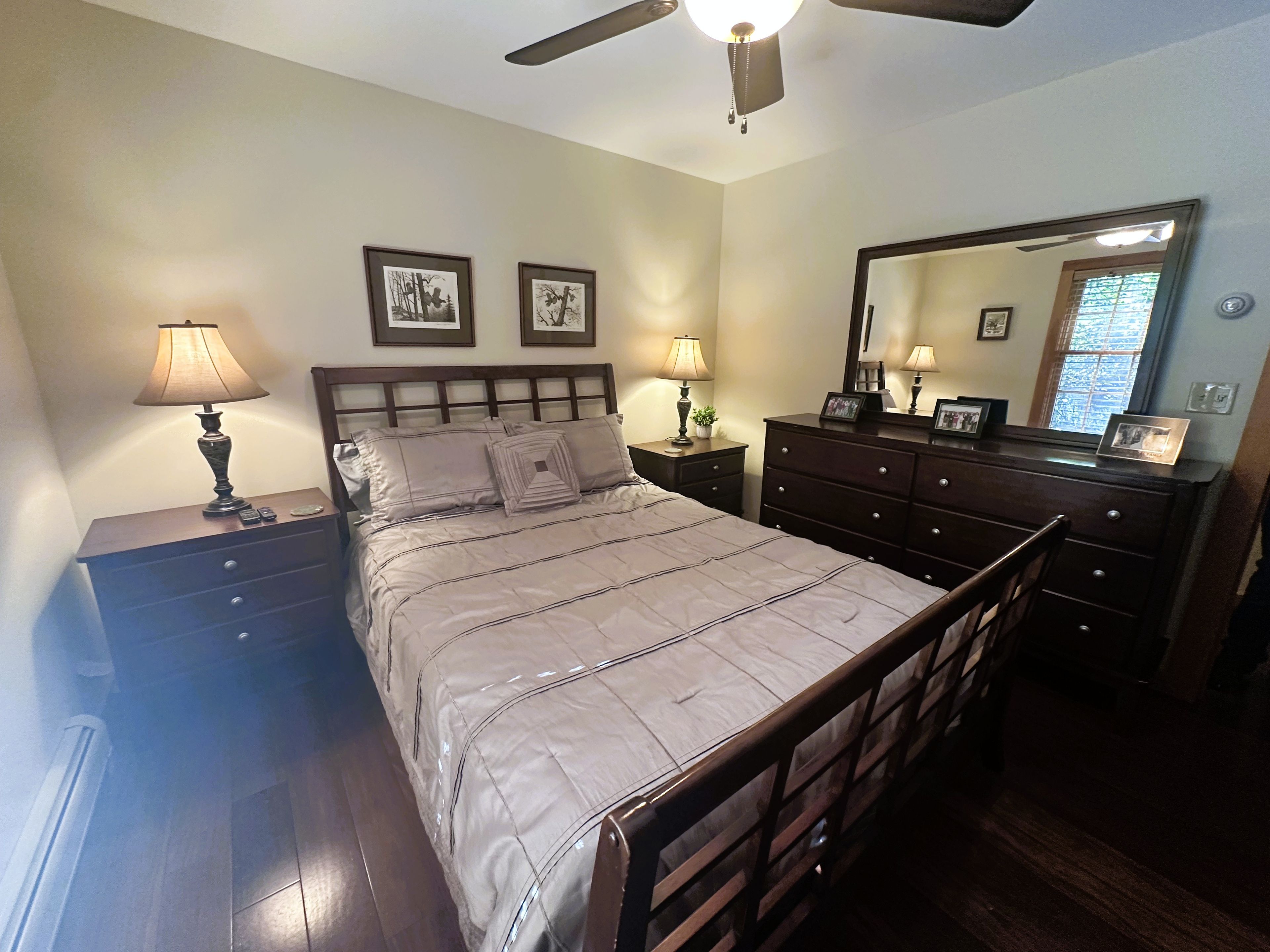 A bedroom with a bed, bedside tables, a dresser, a ceiling fan, and a mirror.