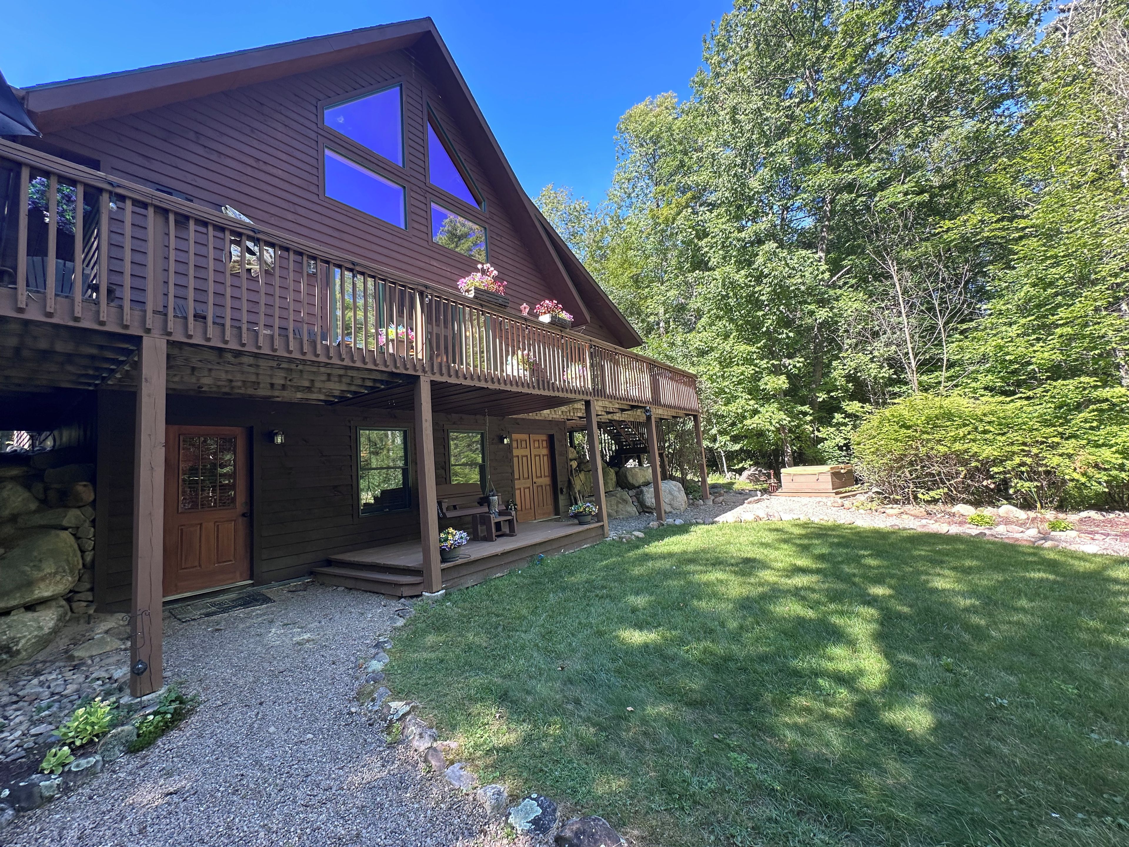 A wooden cabin with a covered porch, stone foundation, and a grassy yard.