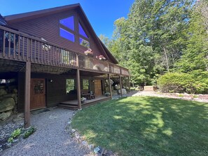 A wooden cabin with a covered porch, stone foundation, and a grassy yard. - Rocky River Chalet - hot tub, apartment, firepit, and Ausable River access (Wilmington)