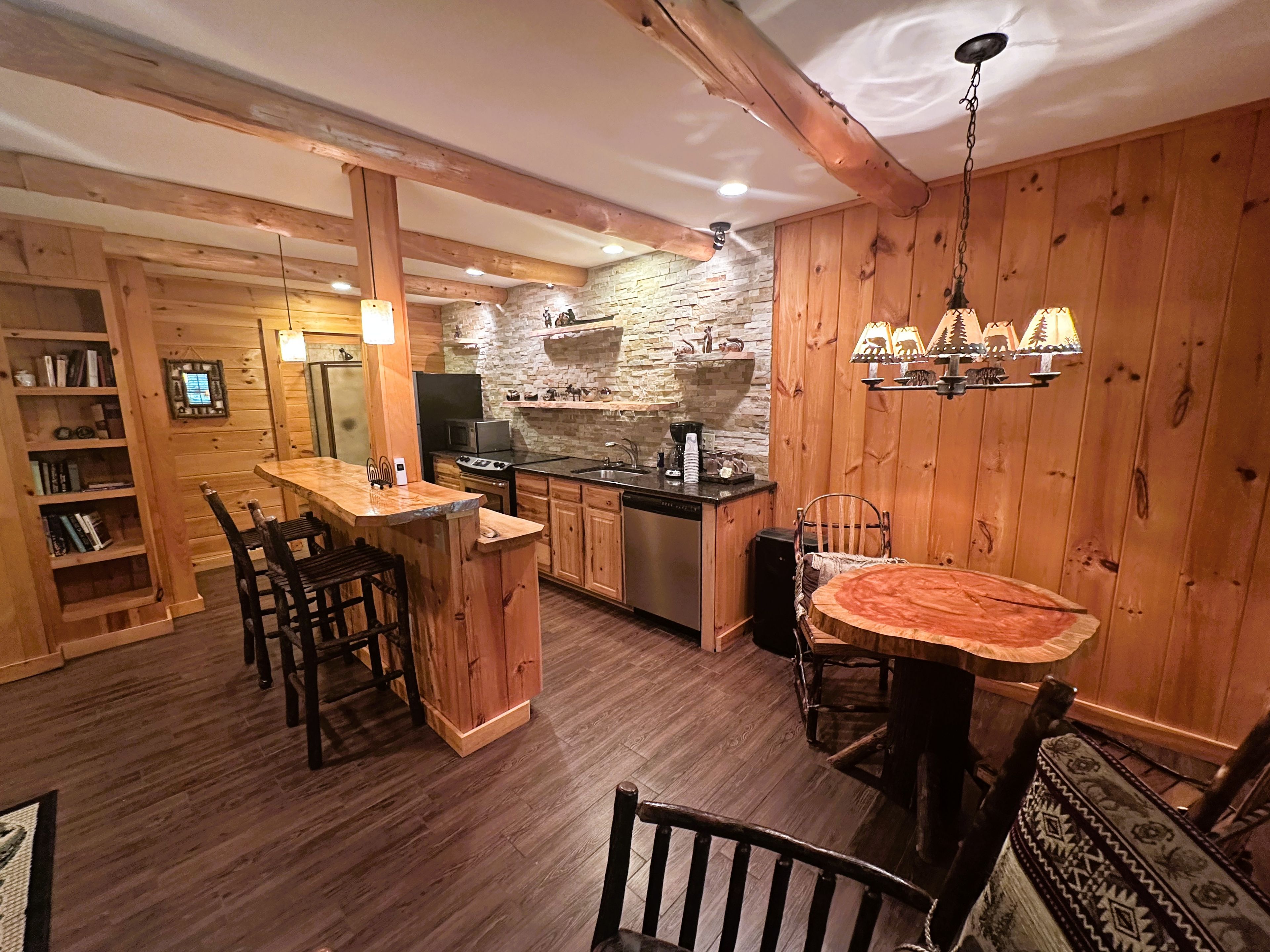Une cuisine rustique avec des poutres en bois, un mur en pierre et un coin repas comprenant une table ronde et des chaises.