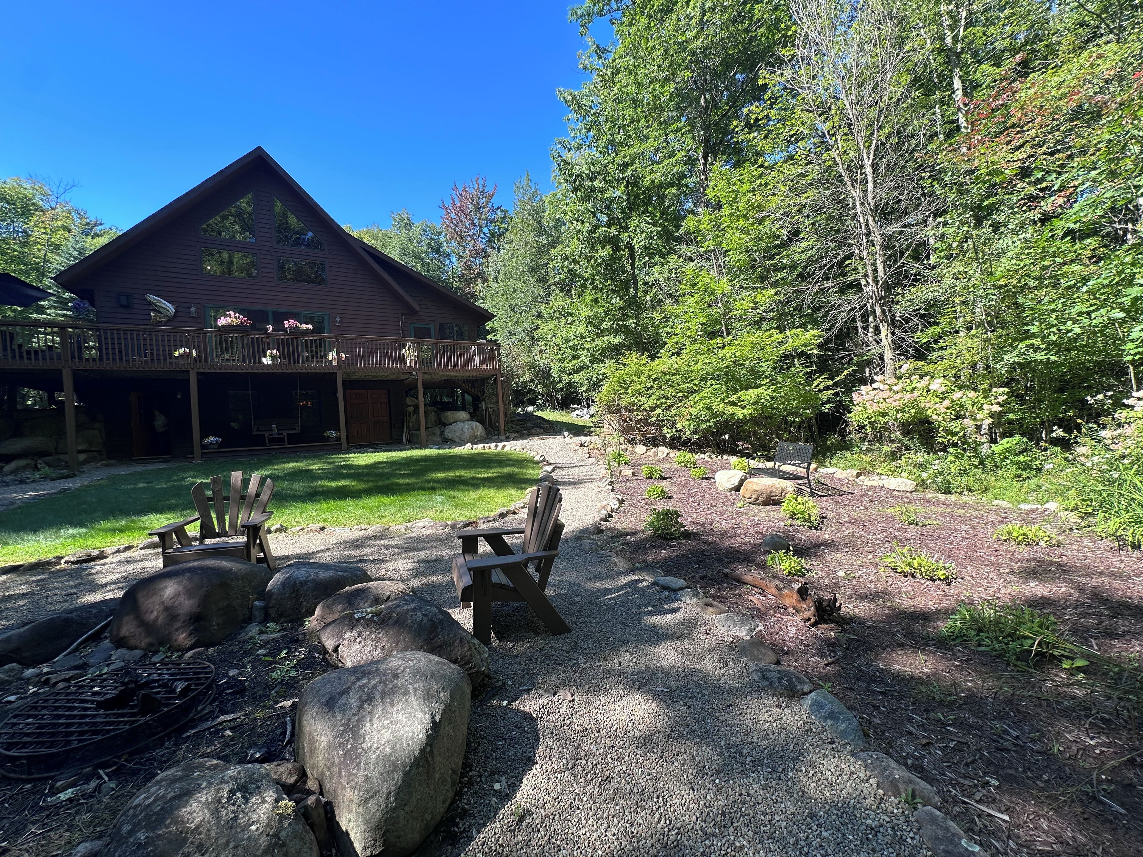 A cabin with a porch, surrounded by a gravel path, and two Adirondack chairs.