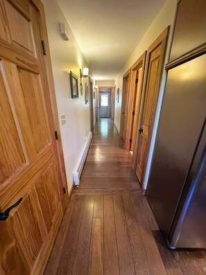 A hallway with wooden doors, a refrigerator, and a light fixture on the wall. - Rocky River Chalet - hot tub, apartment, firepit, and Ausable River access (Wilmington)