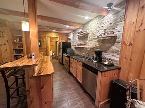 Un interior de madera con una zona de cocina que presenta una pared de piedra, armarios de madera y una mesa de comedor.