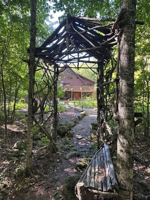 A rustic wooden gazebo in a forested area with a wooden cabin in the background. - Rocky River Chalet - hot tub, apartment, firepit, and Ausable River access (Wilmington)