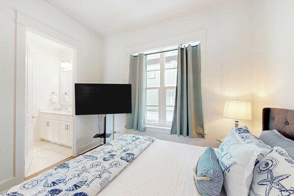 A hotel room with a bed, a television, a window with curtains, and a bedside lamp. - Coastal Vista Retreat | Pet Friendly (Port Aransas)