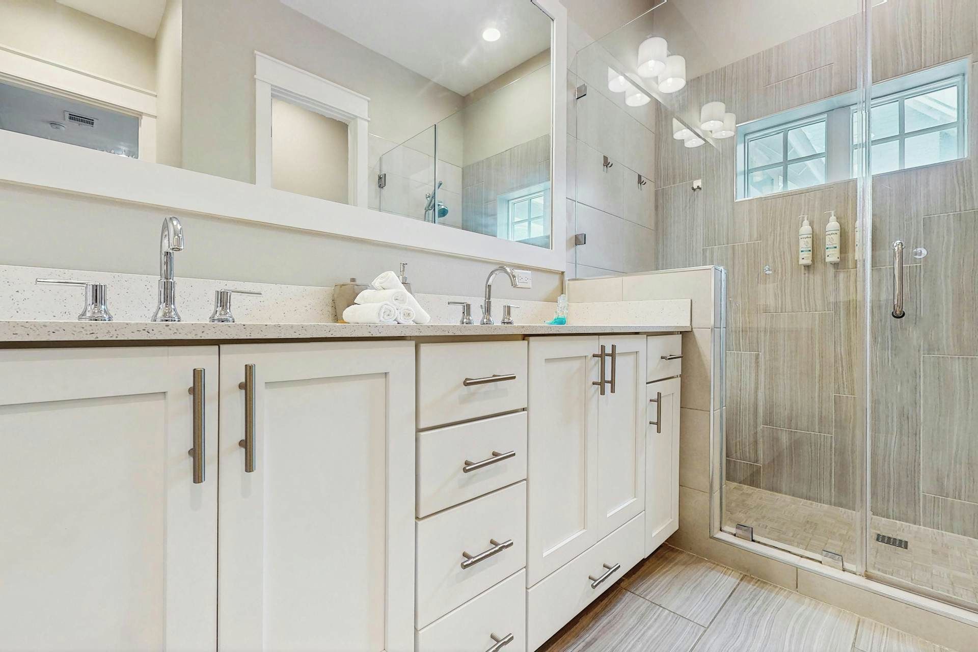 A modern bathroom with a large mirror, a shower enclosure, and a vanity with a sink and multiple drawers.