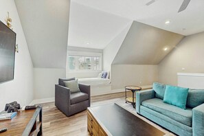 Ein modernes Wohnzimmer mit schrägverdeckter Decke, einer Couch, einem Sessel und einem Couchtisch.