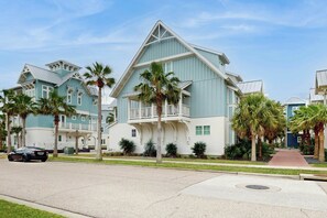 A coastal-style building with a balcony, palm trees, and a clear sky. - Gabby's Retreat | Two Living Areas | Balcony (Port Aransas)