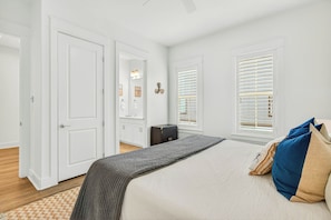 Un dormitorio con cama, cómoda, mesita de noche, ventana con persianas y puerta.