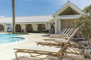 A poolside area with lounge chairs and a building with a sloped roof. - Beach Please | Steps to Beach | Resort Amenities (Port Aransas)