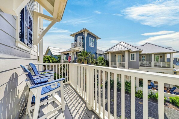 A balcony with a white railing, blue chairs, and a view of neighboring houses. - Gone Breeze | Pet Friendly | Steps to Beach (Port Aransas)