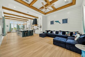 A spacious living area with a wooden ceiling, a large sofa, and a kitchen in the background. - Gone Breeze | Pet Friendly | Steps to Beach (Port Aransas)