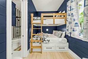Quarto com beliche, janela com cortinas e porta para um banheiro.