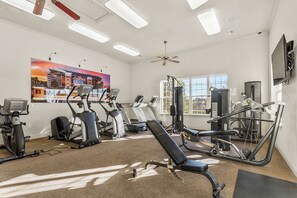 Ein Fitnessraum mit Trainingsgeräten, einem großen Fenster und einem Deckenventilator.