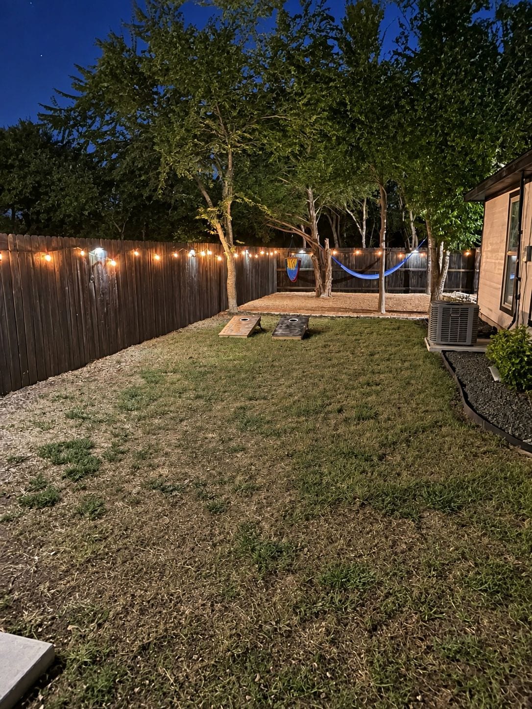 Ein Garten mit Holzzaun, einer Hängematte und einer kleinen Terrassenfläche.