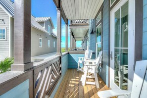 A wooden deck with chairs, a covered area, and a view of the ocean. - Beaches And Bunkers | Golf Views | Pet Friendly (Port Aransas)