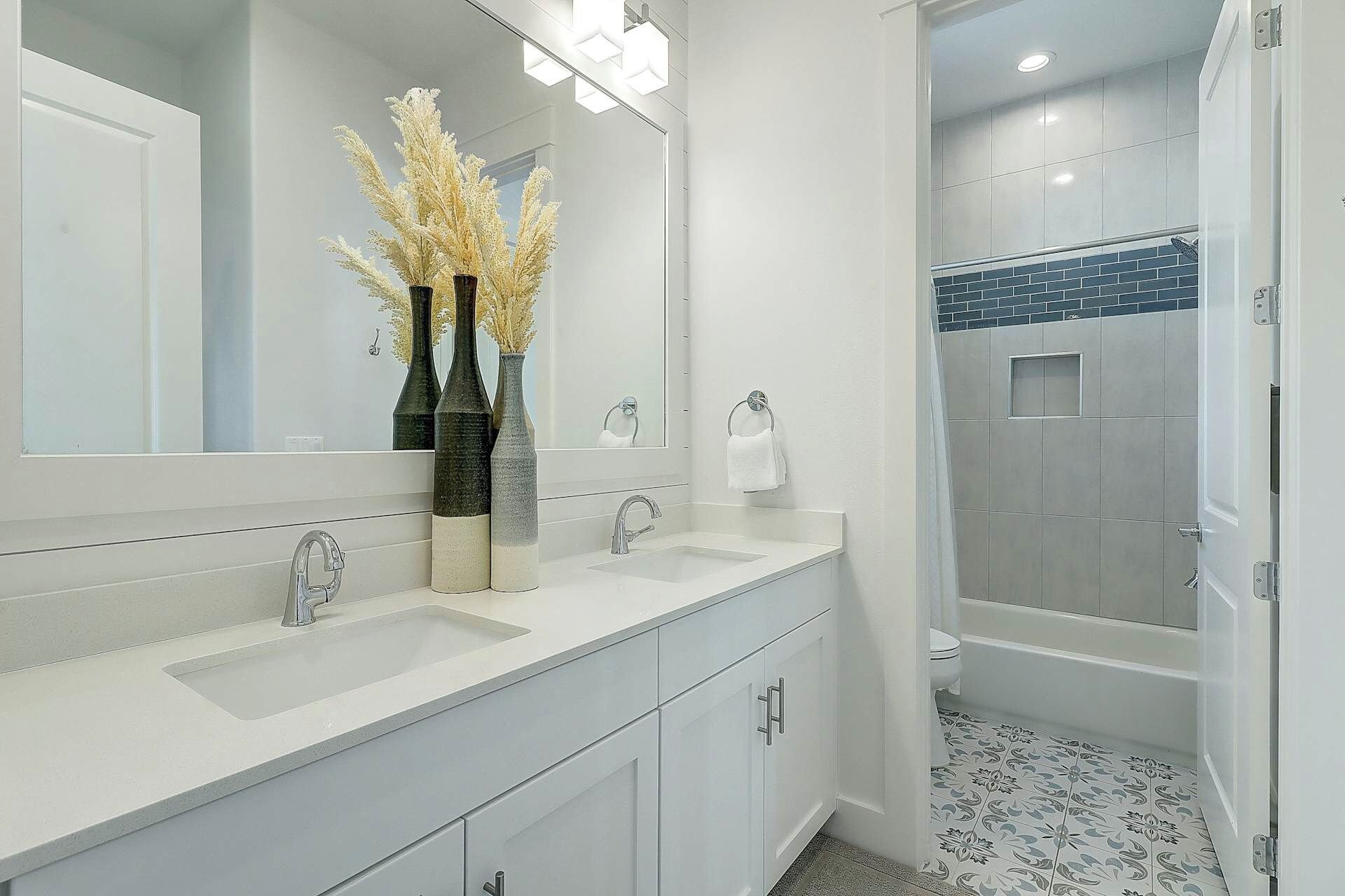 A modern bathroom with a double sink vanity, a large mirror, and a shower area.