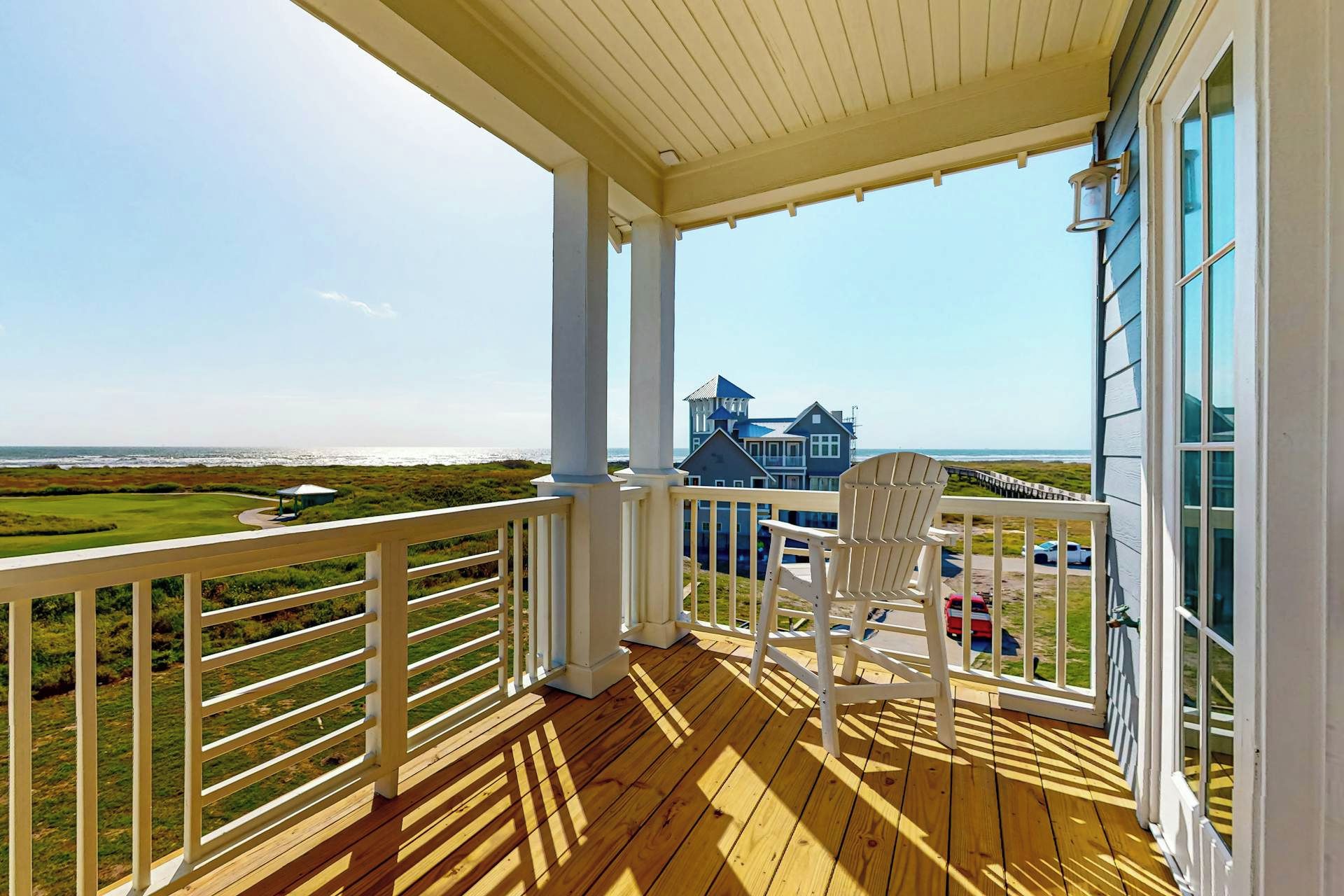 Una terraza de madera con vista a una casa grande y a la playa.