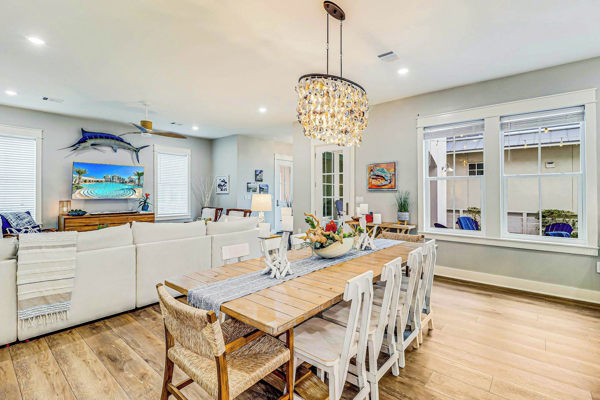 A modern kitchen with a wooden dining table, white chairs, and a chandelier.