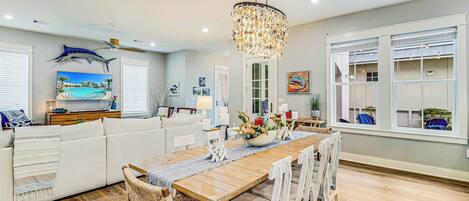 A modern kitchen with a wooden dining table, white chairs, and a chandelier.