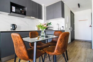 Une cuisine moderne avec des meubles de rangement aux couleurs sombres, une table à manger en verre et quatre chaises marron.