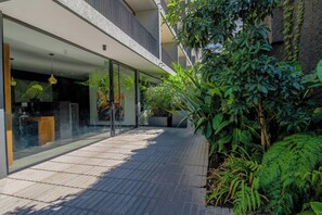 A modern building with a glass facade, outdoor seating area, and lush greenery. - Apartamento 2BR/1BA con Vista Cordillera y Ciudad, Wifi (Santiago)