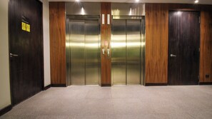 Une paire de portes doubles, dotées d’un panneau en bois et d’une finition métallique, probablement l’entrée d’un ascenseur.
